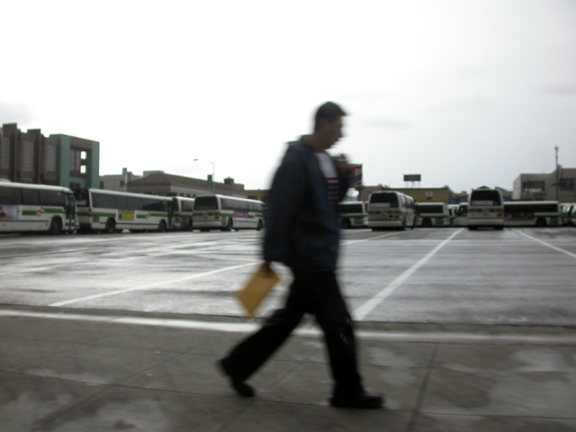 A blurry figure walks by a bus parking lot